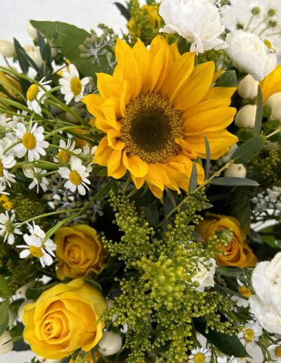 A cheerful bouquet with a bright yellow sunflower, white daisies, and sunny yellow roses