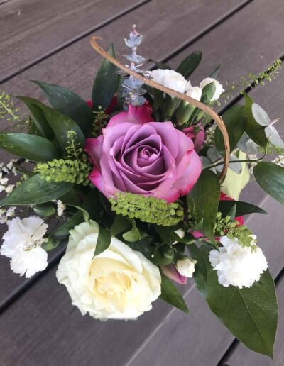 A floral arrangement titled "Small" features a prominent purple rose and a large white rose, surrounded by smaller white flowers, green leaves, and stems. The bouquet rests on a wooden surface.