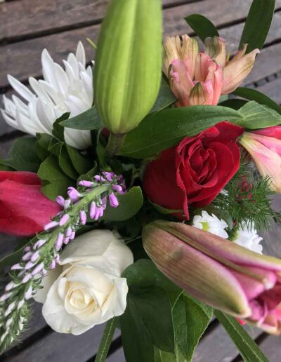 A delightful bouquet named "Small," featuring an array of vibrant flowers including red roses, white roses, pink tulips, and other assorted blooms with green leaves as accents, all beautifully arranged on a wooden surface.