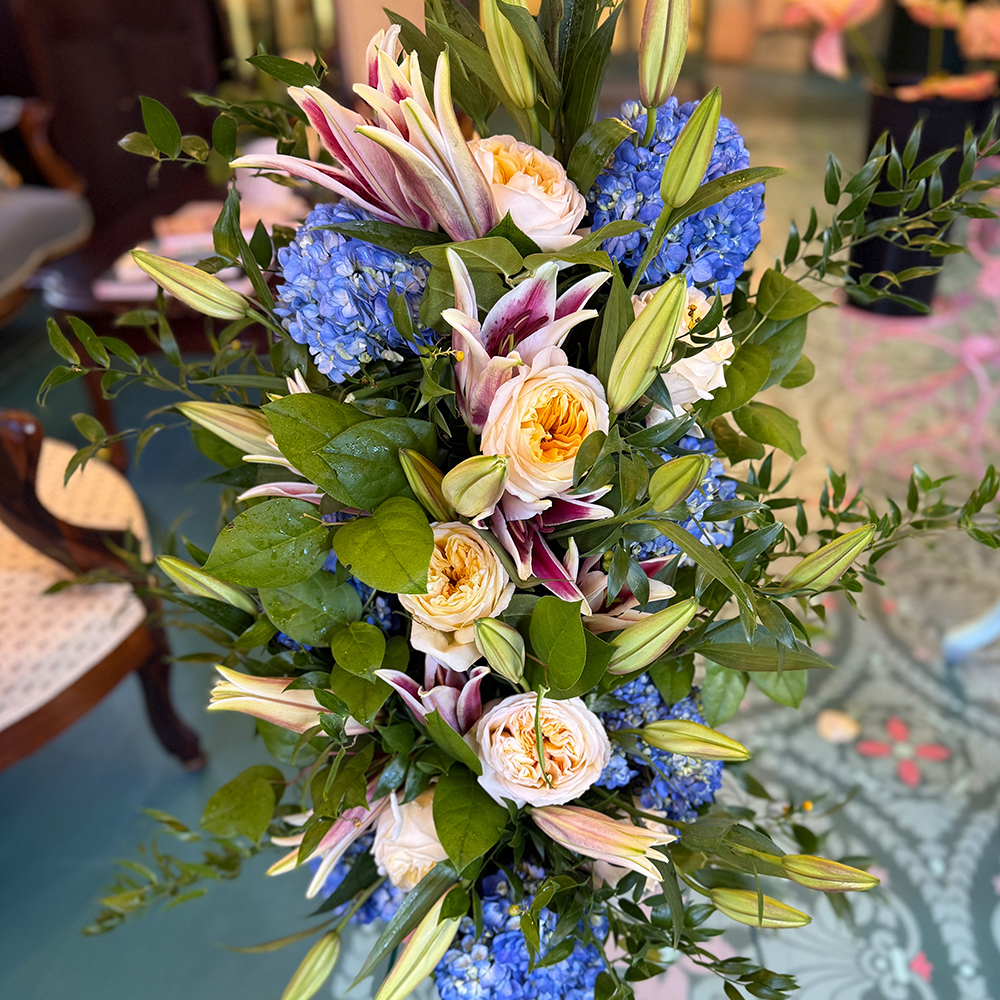 A vibrant bouquet featuring large yellow roses, smaller yellow roses, white blossoms, and lush green foliage. The flowers are artistically arranged in a natural style, creating a fresh and cheerful display. Introducing Medium, the perfect arrangement for any occasion.