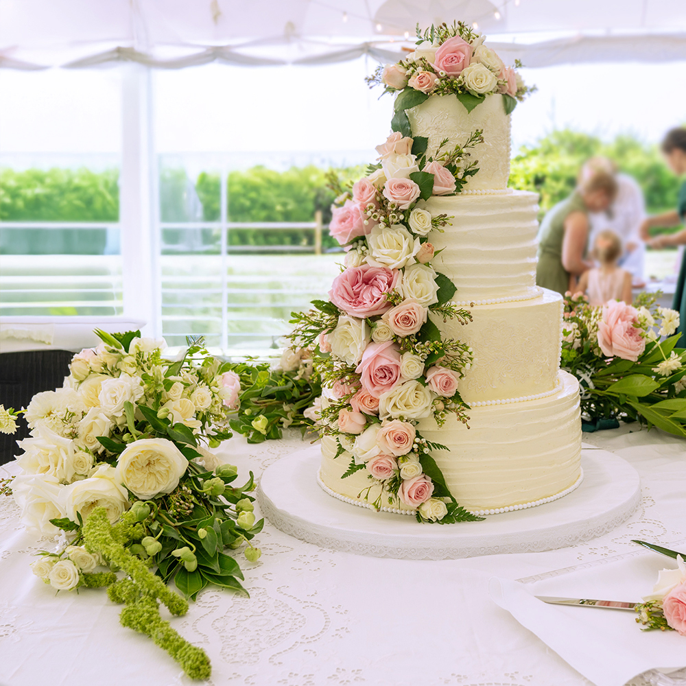 A vibrant bouquet featuring large yellow roses, smaller yellow roses, white blossoms, and lush green foliage. The flowers are artistically arranged in a natural style, creating a fresh and cheerful display. Introducing Medium, the perfect arrangement for any occasion.